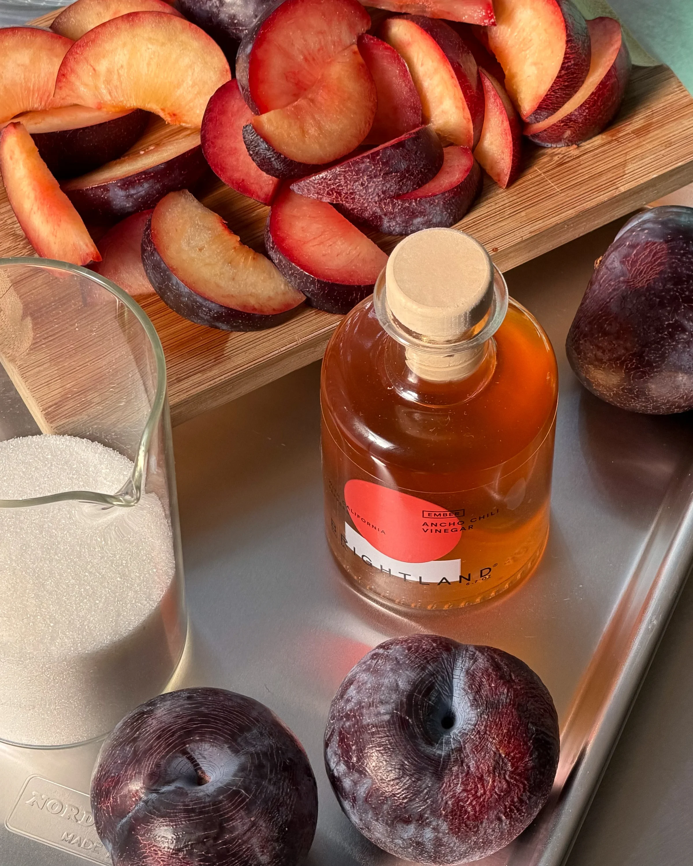 Sliced plums and a bottle of vinegar on a kitchen counter
