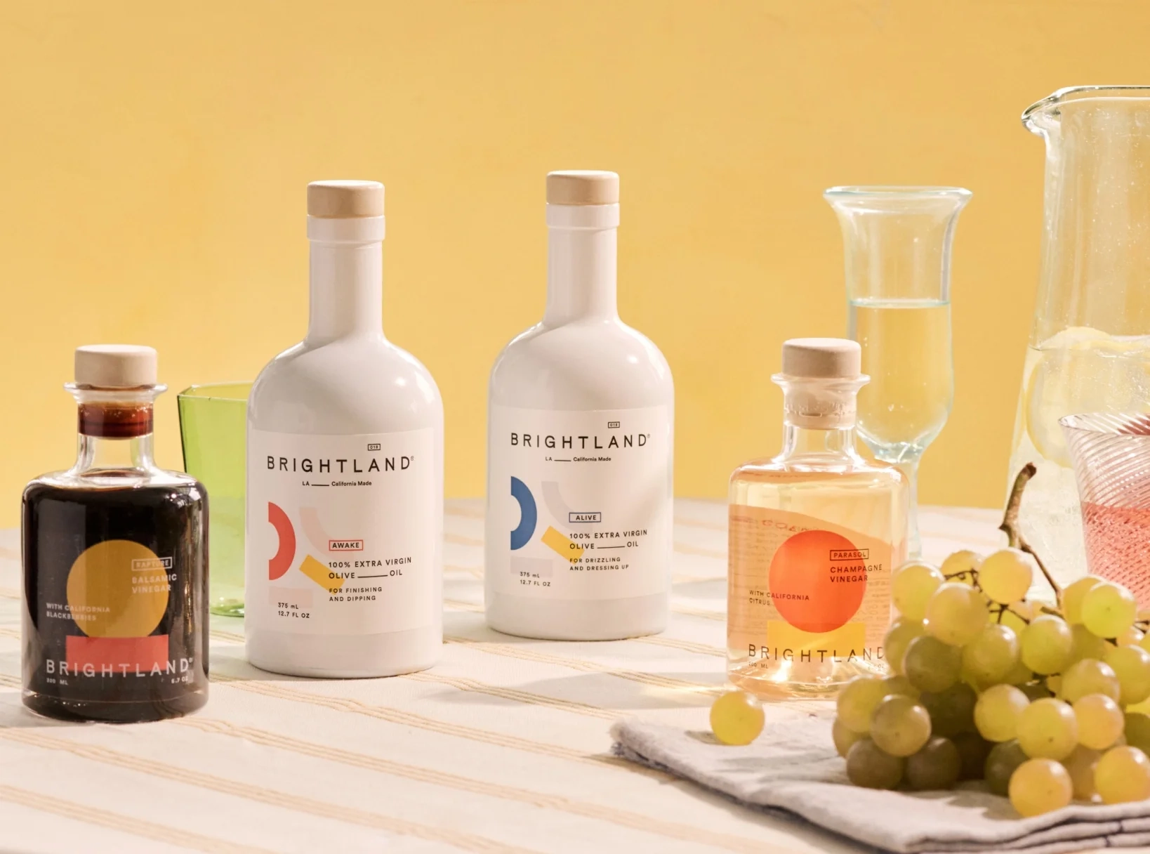 Brightland bottles of olive oil and vinegar beside a bunch of grapes
