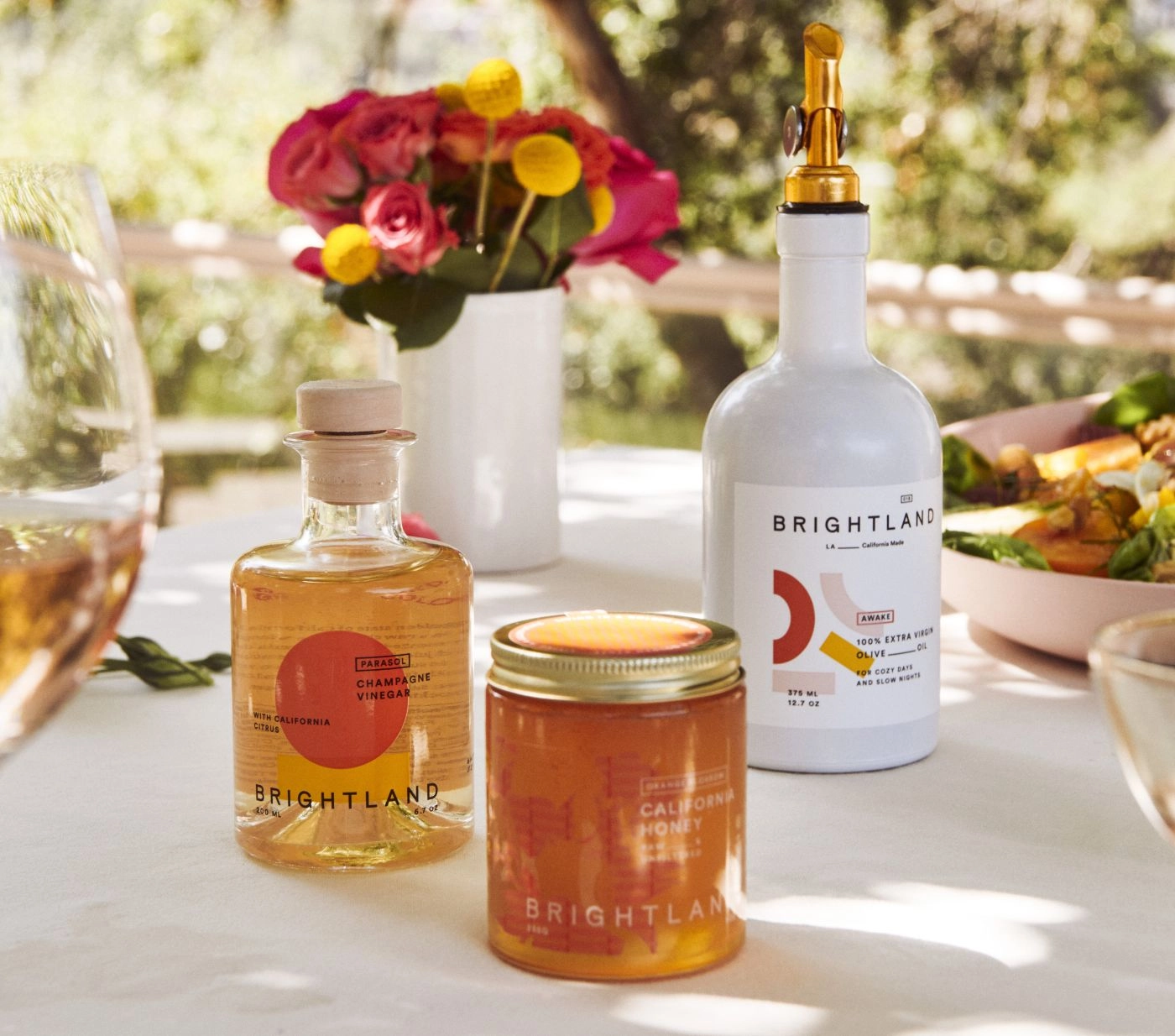 A table in the sun with flowers, honey and a Brightland bottle